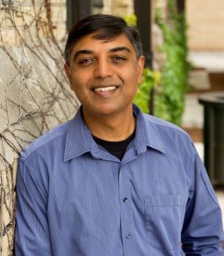 A male with brown skin and black hair, smiling
