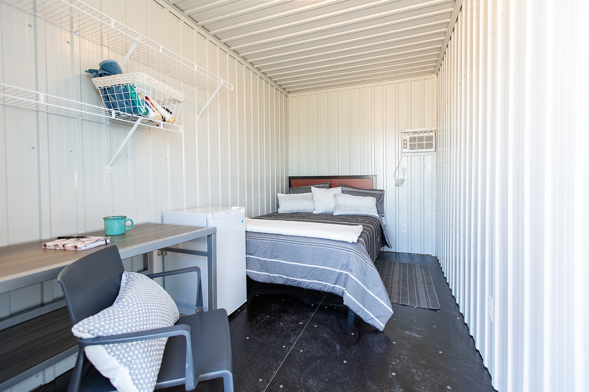 An interior shot of one of the cabins shows a bed with bedding, desk, chair and mini fridge. 