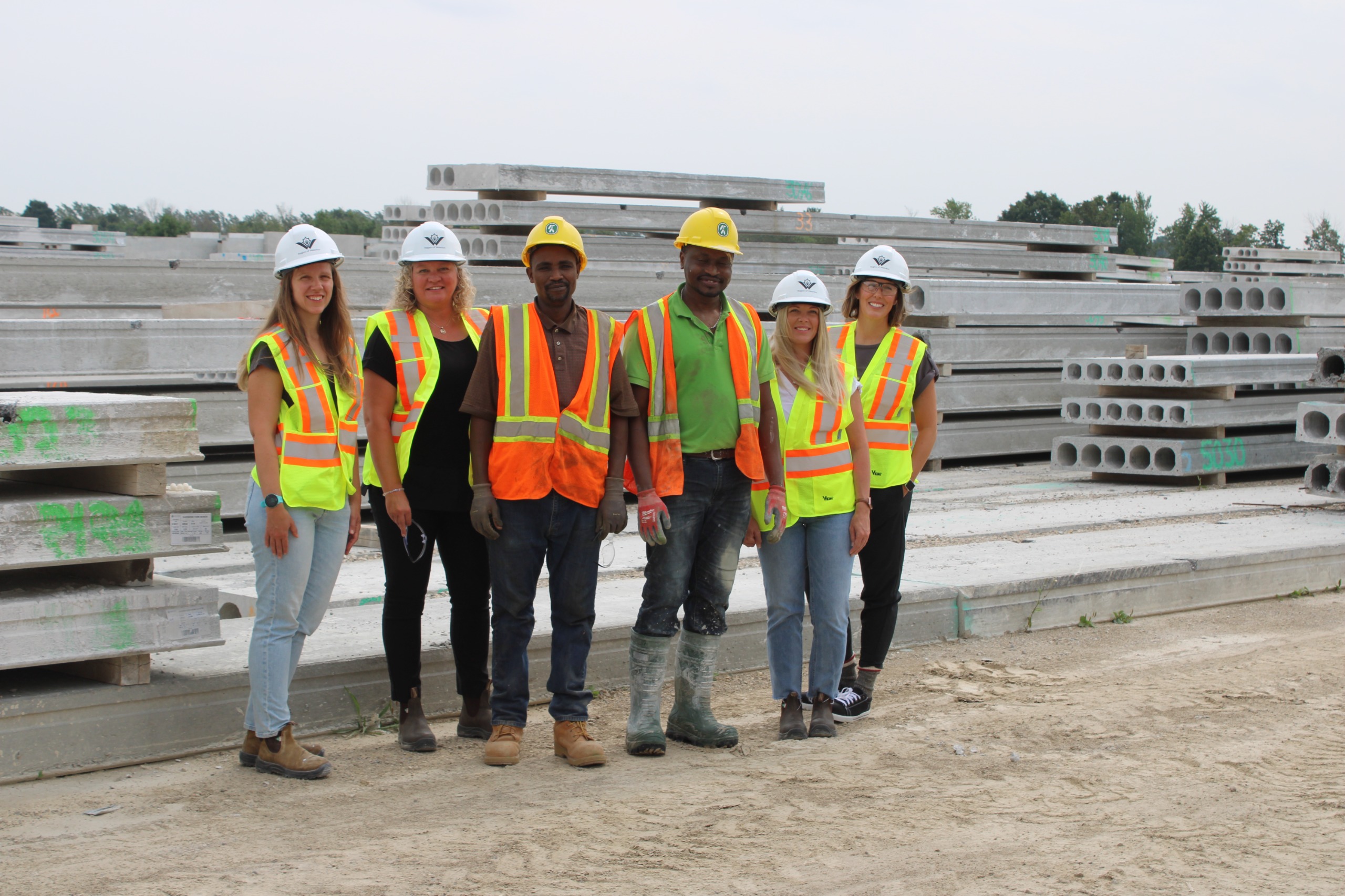 People supporting and participating in the Grand Valley Construction Association Path to Employment in Construction program are wearing construction hats and vests and standing at a construction site. 