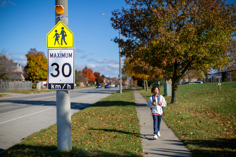 A boy walks to school near a school safety sign zone.