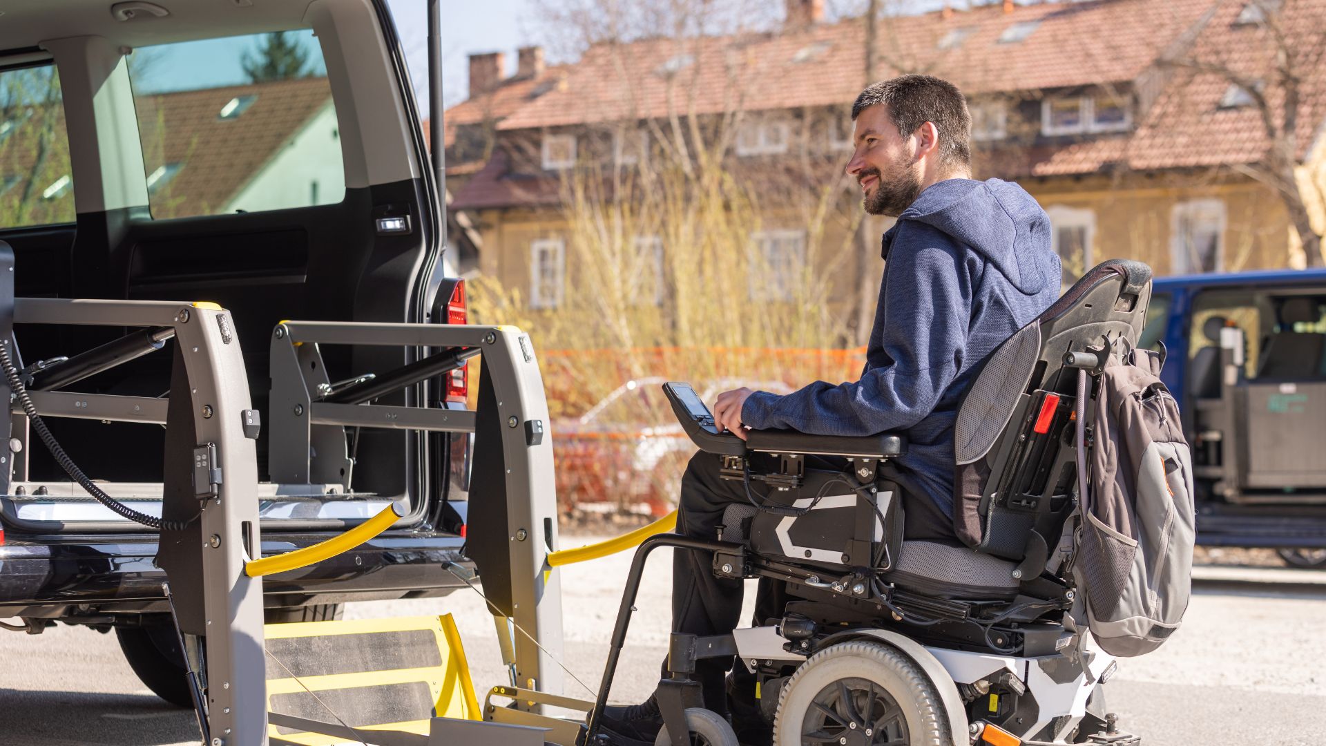 A man using a power chair drives up to a an accessible vehicle lift.
