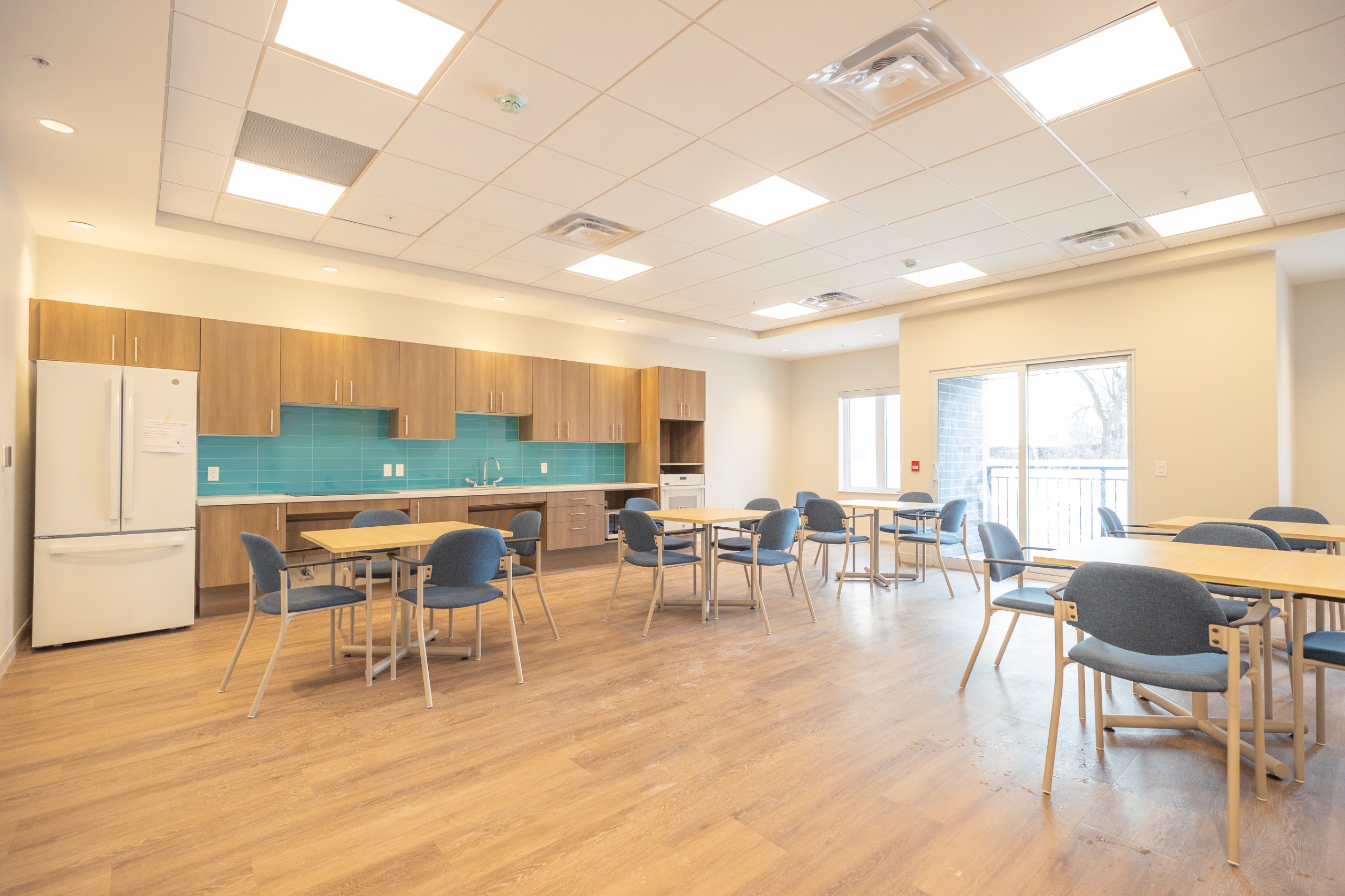 image of an amenity room with tables, chairs, a kitchen counter and cooktop