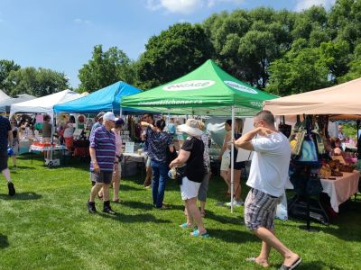 Tent with green canopy and Engage Kitchener logoat Cherry Festival. Several people are crowded around the tent looking inside. 
