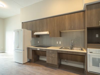 image of the kitchen area of an accessible unit which shows a white fridge, brown wood cupboards and a roll-under countertop